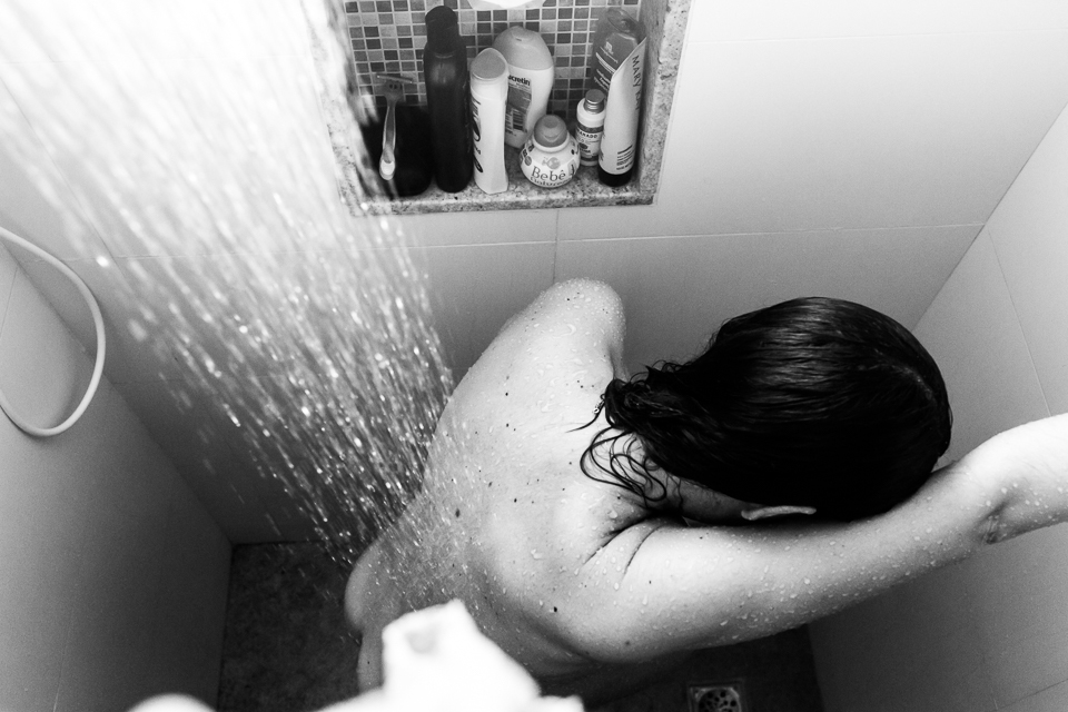 gestante no chuveiro deixa a água quente cair nas costas para aliviar as dores das contrações 