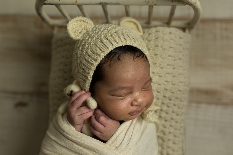 Newborn no tablado de demolição do leo moreno usando usando touquinha da mimos de fotos e segurando ursinho da reinado kids 