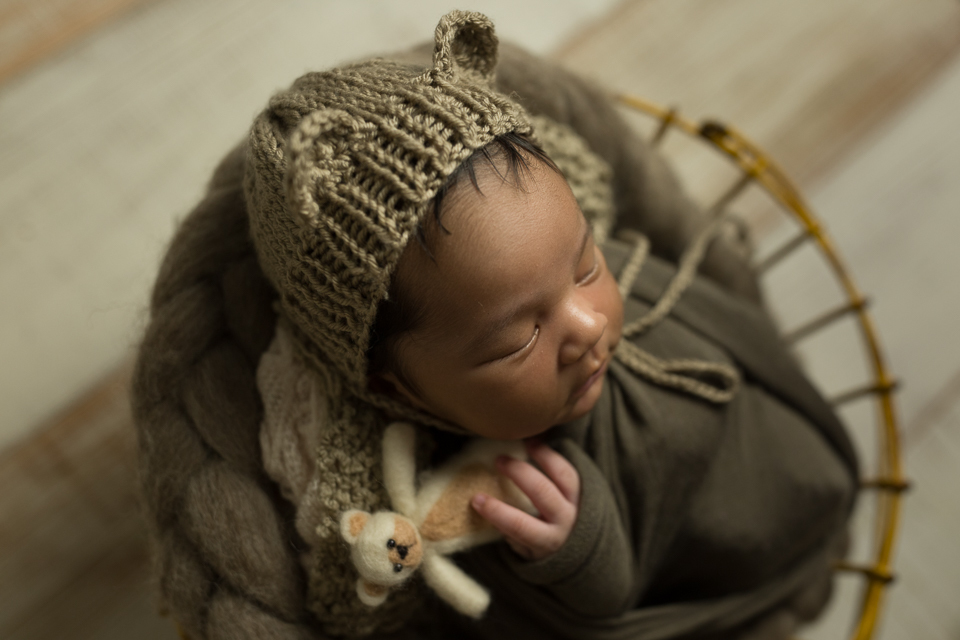 Newborn segurando ursinho da reinado kids e com touquinha no cestinho da love prop 