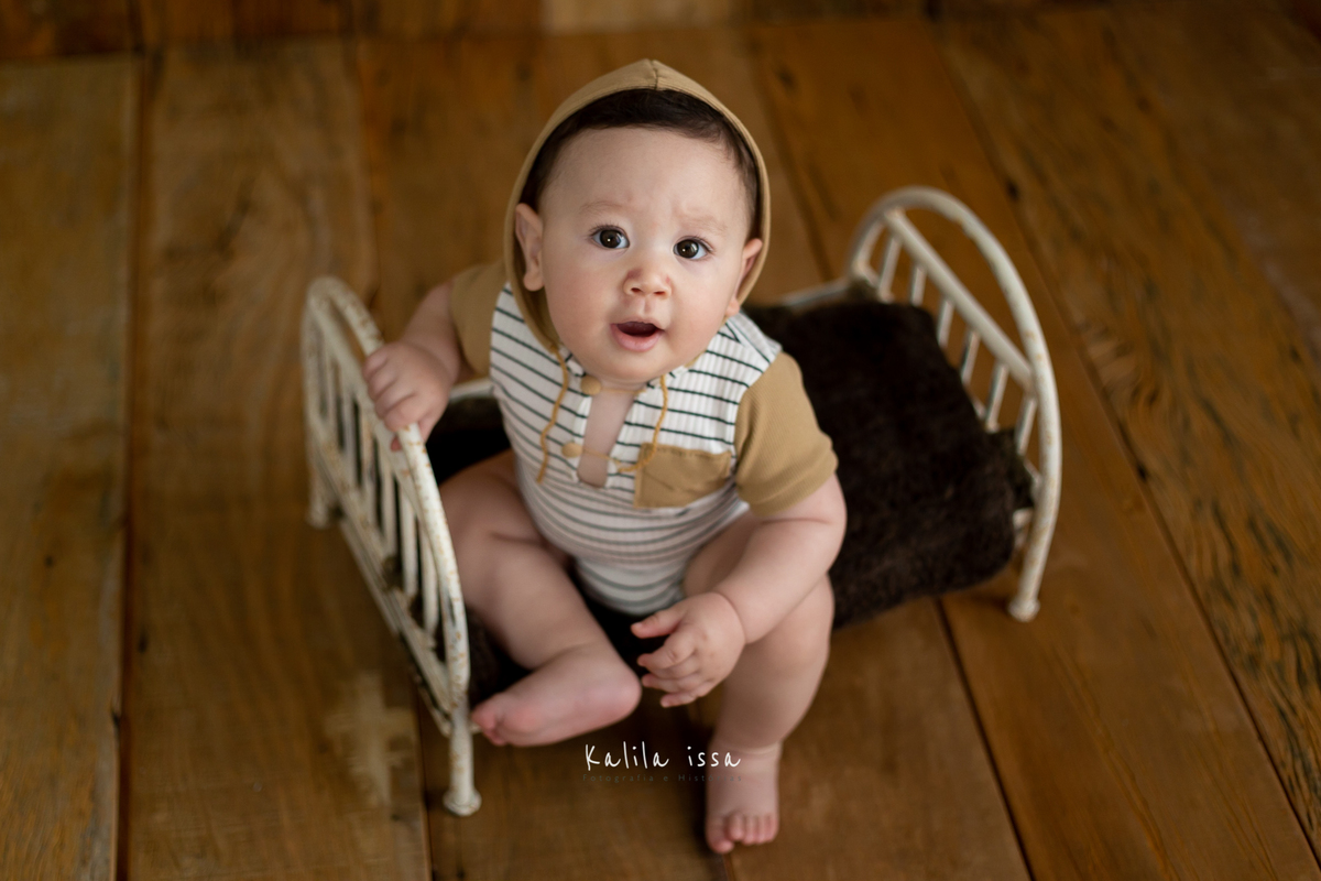 bebê de 8 meses sentado na caminha de ferro da love love prop e usando roupinha da reinado kids