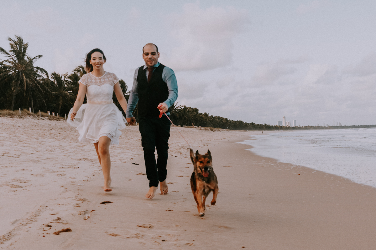 casal correndo na praia com cachorro