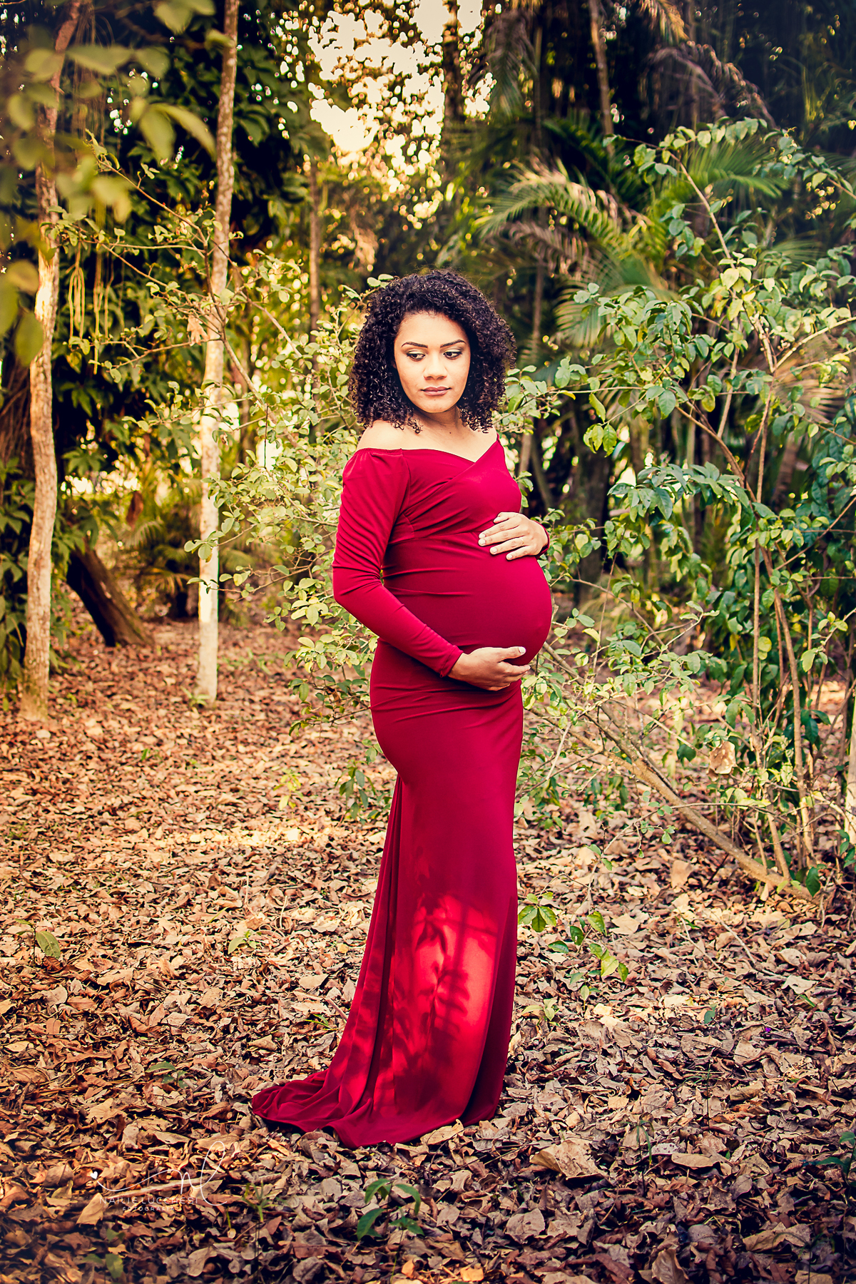 ensaio gestante realizado em são jose dos campos no parque vicentina aranha, na foto tem um gestante de pele negra e cabelos cacheados com um lindo vestido longo e vermelho e ela esta feliz