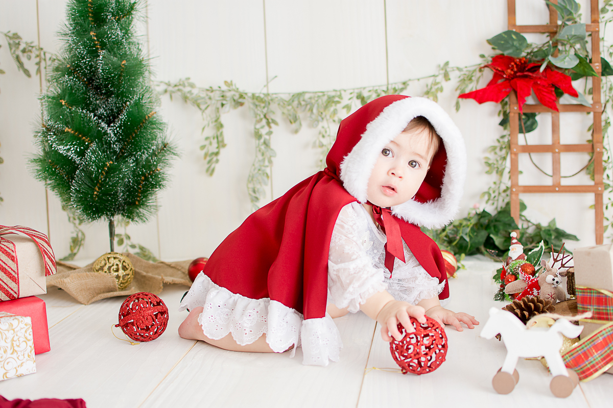 uma menina linda e vestida de vermelho, brincando no ensaio de natal, ela esta com uma bola de natal