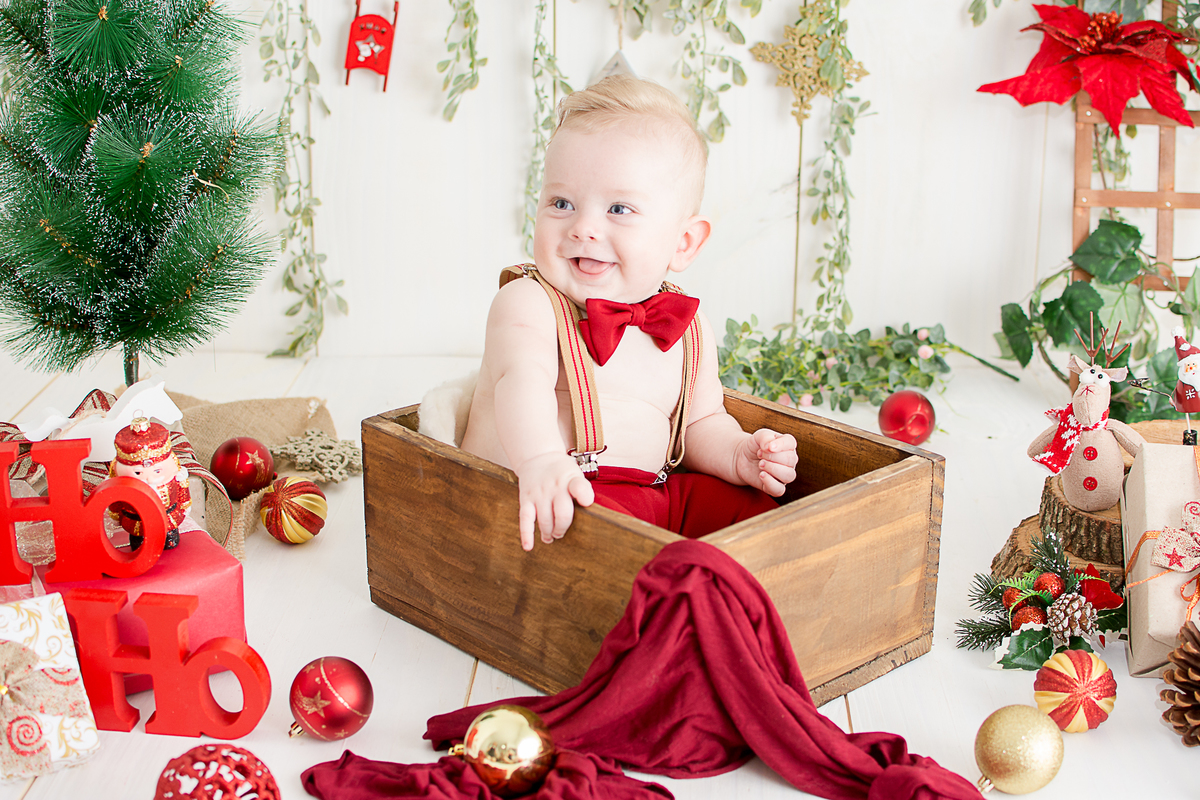 um menino com 6 meses de vida, usando calça e suspensório e gravata borboleta, ele esta sorrindo no estúdio nailie lucchesi