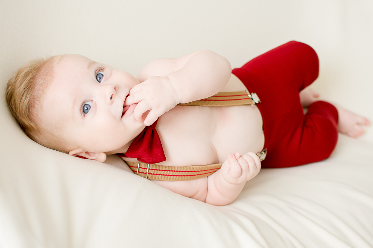 um bebe lindo com 6 meses, um menino vestido de vermelho com a mão na boca, loiro de olhos azuis