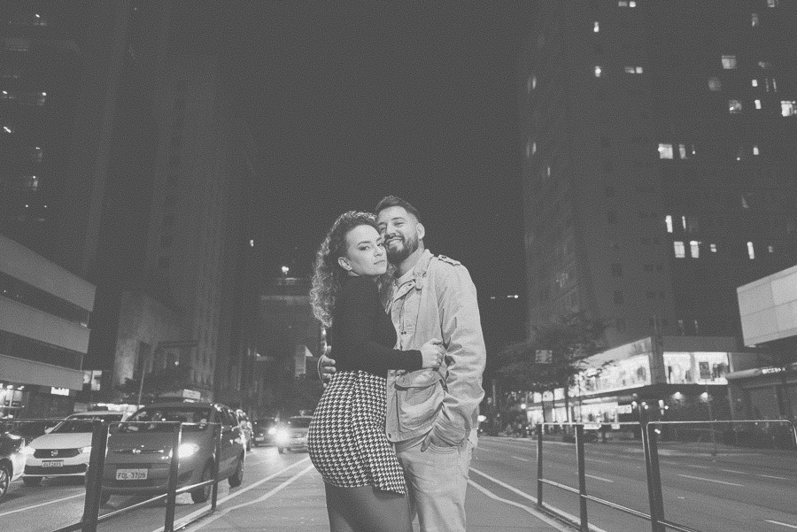 Ensaio urbano noturno na Avenida Paulista: fotografia artística em preto e branco do casal abraçado com prédios de SP ao fundo