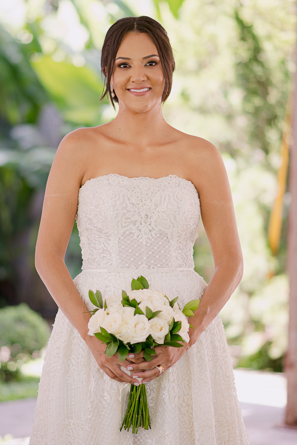 Beleza radiante! A noiva posa sorridente com seu buquê de rosas brancas nos jardins do Recanto Serimbura. O vestido tomara que caia bordado destaca a elegância clássica deste casamento em São José dos Campos.