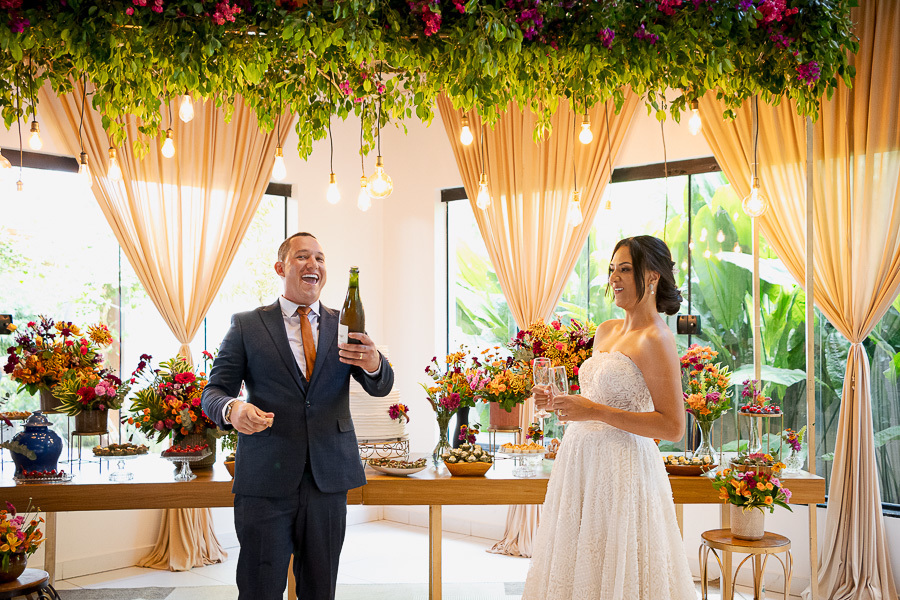 A festa começou! A alegria contagiante do noivo abrindo a bebida ao lado da noiva na recepção no Recanto Serimbura. Celebração inesquecível em um cenário deslumbrante em SJC.