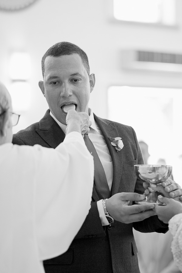Momento sagrado. O noivo recebe a hóstia consagrada durante a missa de casamento. Fotografia P&B que registra a fé e a seriedade do compromisso na Paróquia Espírito Santo.
