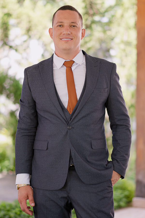 Elegância masculina. Close nos detalhes do terno azul texturizado e gravata terracota. A combinação perfeita para noivos modernos que buscam estilo em casamentos de dia.