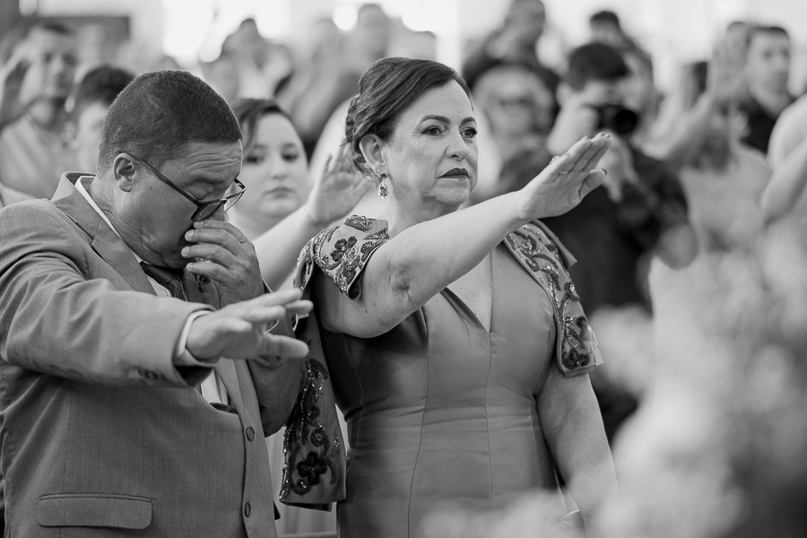 A força da família. Pais emocionados estendem as mãos para abençoar a união dos filhos. Um registro preto e branco poderoso de fé e amor na cerimônia em São José dos Campos.