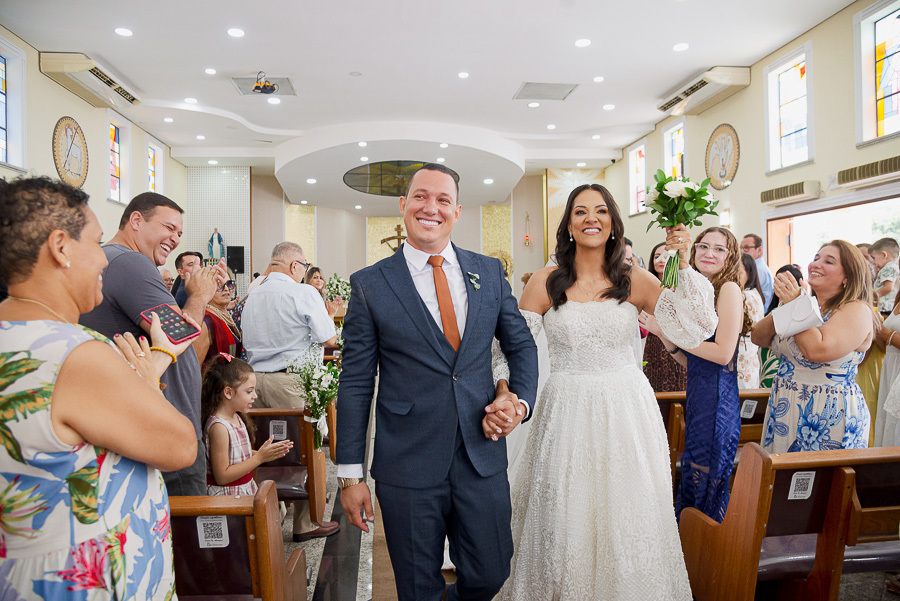 Casados e radiantes! A noiva ergue o buquê celebrando o amor na saída da Paróquia Espírito Santo. Destaque para o caimento impecável do vestido em movimento.
