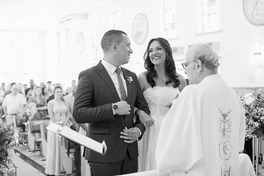 O olhar apaixonado do noivo diz tudo. Início da emocionante cerimônia de casamento na Paróquia Espírito Santo em SJC, com o padre abençoando a união do casal.