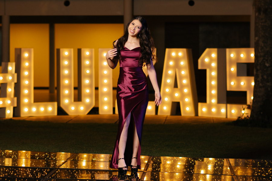 Ensaio de 15 anos deslumbrante! A debutante posa em um elegante vestido longo vinho em frente ao letreiro luminoso personalizado 