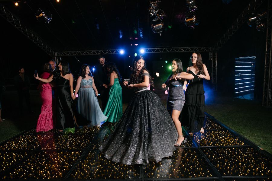 Diversão total no Espaço JK Jacareí! A debutante e suas amigas apontam e brincam na pista de dança, criando uma cena cheia de energia e descontração na festa de 15 anos.