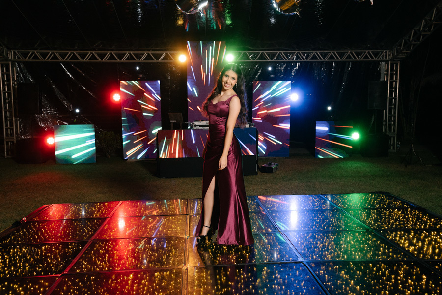 Pronta para a festa! A debutante posa na pista de dança iluminada, destacando seu vestido longo e a produção incrível do evento. Um clique que valoriza a cenografia e a protagonista da noite.