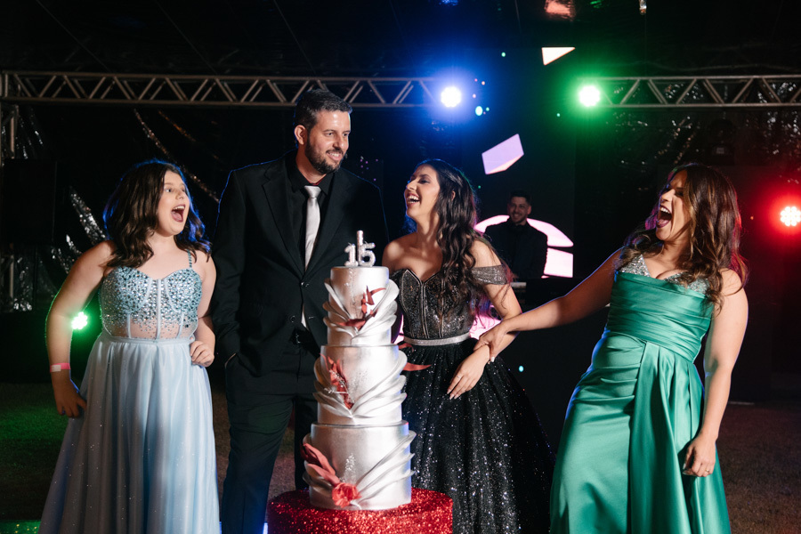 Detalhes que encantam: a debutante posa junto à mesa do bolo em sua festa. Destaque para a decoração sofisticada com iluminação moderna. Inspiração para 15 anos.