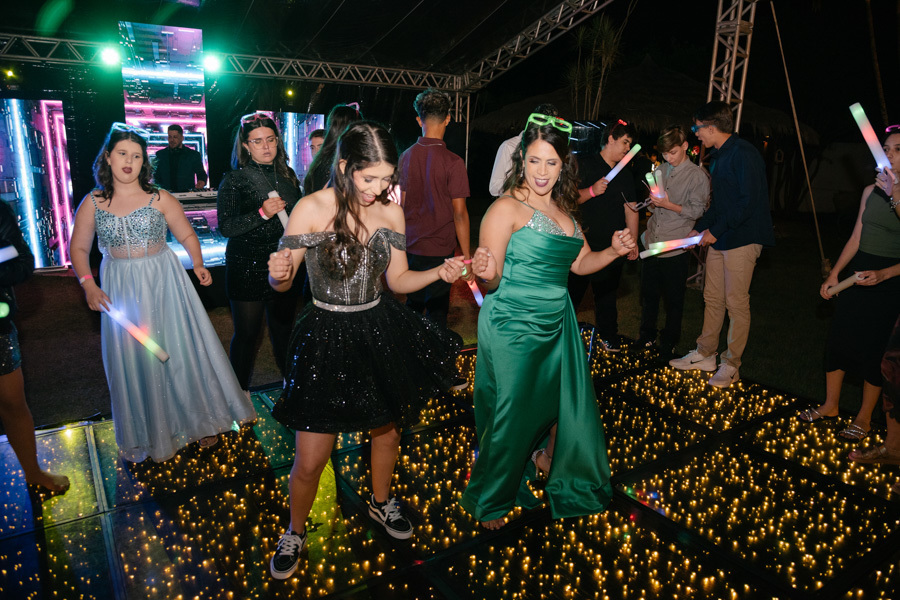 A festa explodiu! Muita energia na pista com bastões de LED. A técnica fotográfica capta o movimento e a vibração frenética da debutante e suas amigas curtindo a balada intensamente.