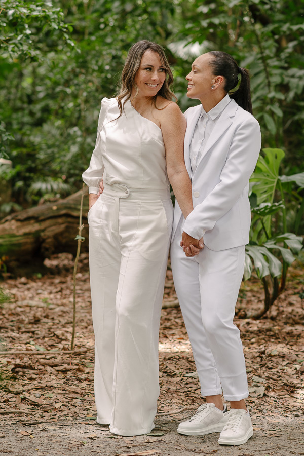 A beleza está nos detalhes. Um close que valoriza a textura dos trajes e a delicadeza das mãos unidas, complementando a história visual do casamento.