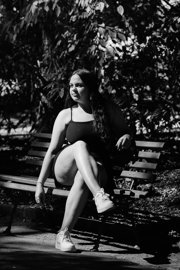 Poses para ensaio feminino: Camila sentada confortavelmente no banco do parque. Dicas de direção para fotos de 15 anos naturais.