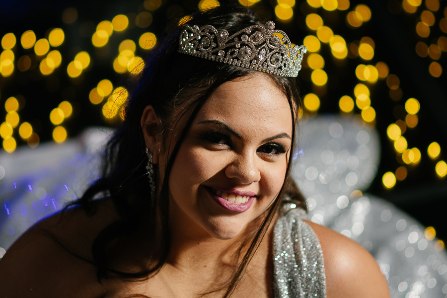 Retrato noturno: O sorriso da debutante em destaque com o fundo desfocado pelas luzes da festa.