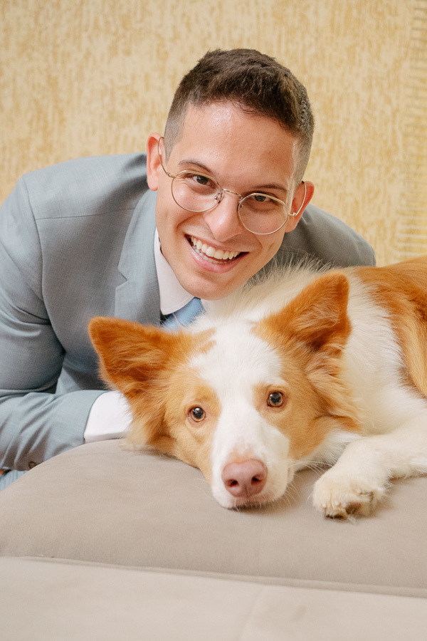 Noivo Marcus sorrindo espontaneamente ao lado de seu cachorro Border Collie durante os preparativos. Retrato leve e divertido do making of masculino, mostrando a felicidade e a conexão com o pet antes do casamento.