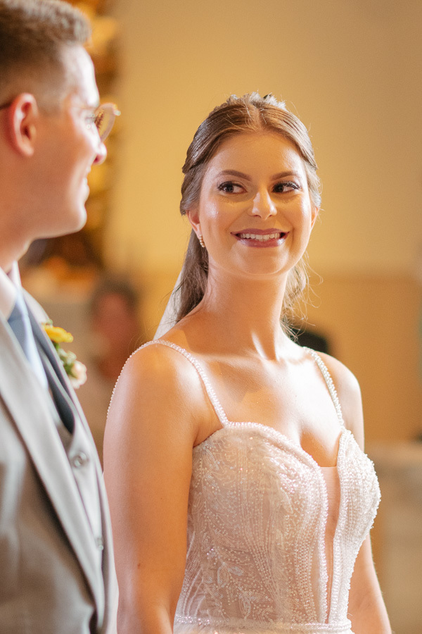 Noiva Isabelle sorrindo radiantemente para o noivo Marcus no altar. Close que captura a troca de olhares apaixonados e a cumplicidade do casal durante a cerimônia no Parque Vicentina Aranha. O amor visível em cada detalhe.