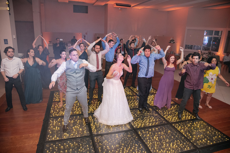 Flash mob animado com os noivos e convidados na pista de dança. A energia contagiante da festa na APVE Embraer, com todos fazendo a coreografia no piso de LED. Momentos de pura diversão e conexão com amigos e família.