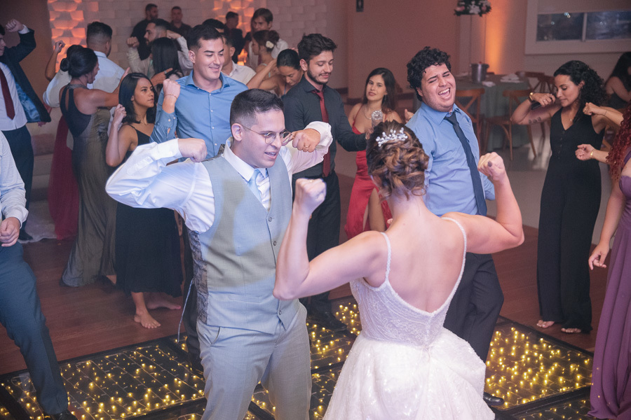 Noivos Marcus e Isabelle brincando e fazendo poses divertidas na pista de LED com os padrinhos. Festa de casamento animada na APVE Embraer, capturando a energia, a descontração e a coreografia espontânea dos recém-casados.