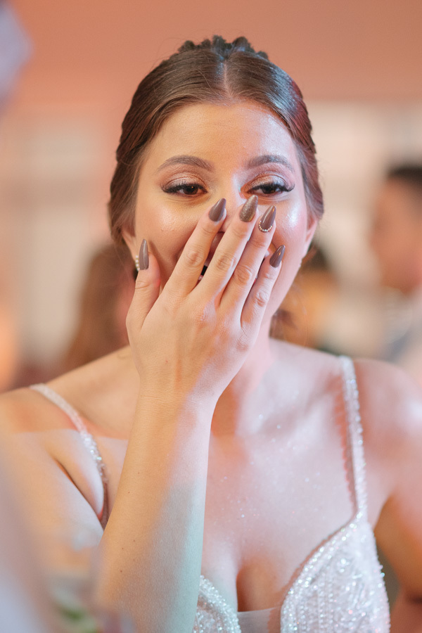 Close da noiva Isabelle rindo emocionada, cobrindo o rosto com as mãos. Destaque para os detalhes das unhas e a maquiagem intacta durante a festa. Um flagra autêntico da felicidade e das emoções à flor da pele.