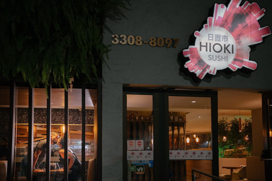 Ensaio pré-wedding de Tainara e Juliano na fachada do Hioki Sushi em São José dos Campos. Fotógrafo de casamento em SJC e Vale do Paraíba registrando histórias em locais afetivos. Foto de casal urbana e noturna. Inspire-se para o seu ensaio!