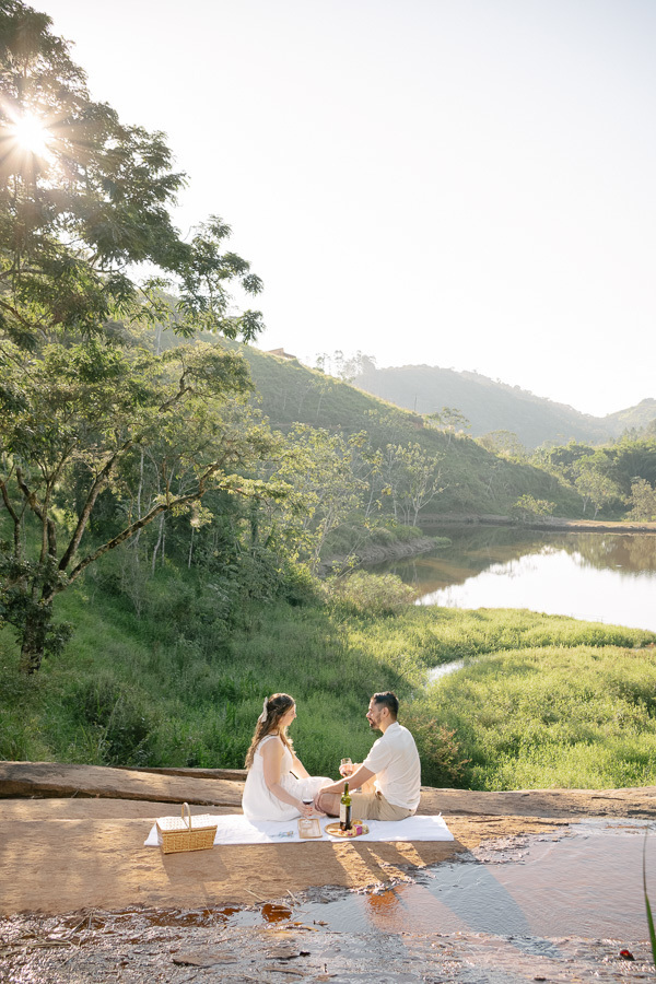 Piquenique no ensaio pré-wedding de Tainara e Juliano em SJC. Fotógrafo de casamento em São José dos Campos e Vale do Paraíba focado em estilo lifestyle e conexão na natureza. Foto de casal espontânea à beira do lago. Inspire-se para seu ensaio!