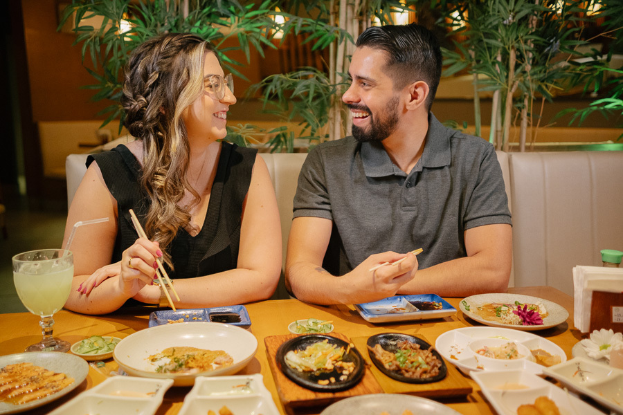 Tainara e Juliano sorrindo durante jantar no Hioki Sushi em SJC. Ensaio pré-wedding lifestyle em São José dos Campos. Fotógrafo de casamento no Vale do Paraíba capturando a alegria e momentos reais do casal em seu restaurante favorito.