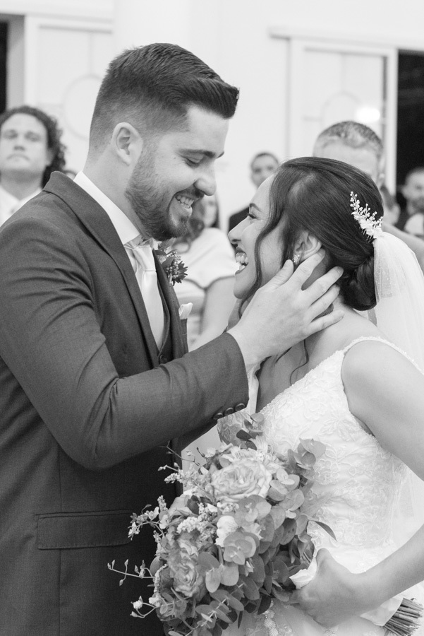 Close em preto e branco do carinho entre os noivos no altar. Lucas acaricia o rosto de Gabriela, que sorri emocionada. Fotografia artística e atemporal que captura a conexão íntima do casal durante a cerimônia.
