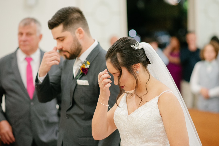 Lucas e Gabriela não contêm as lágrimas de emoção no altar. Noivos chorando juntos durante a cerimônia na Capela Nossa Senhora de Fátima. Fotografia documental que registra a sensibilidade e a verdade do amor no casamento.