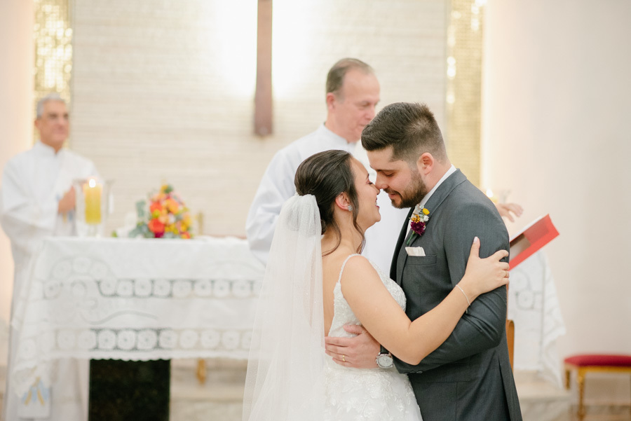 Lucas e Gabriela encostam as testas sorrindo após os votos. Um gesto de profunda conexão, intimidade e carinho no altar. O alívio e a alegria de estarem oficialmente casados na Capela Nossa Senhora de Fátima.