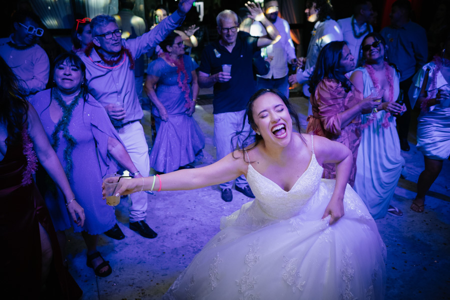 Noiva Gabriela cantando e dançando com toda energia na pista. Iluminação de festa colorida e vibração lá em cima na Quinta das Palmeiras. Fotografia que captura a alegria contagiante da noiva aproveitando cada segundo.