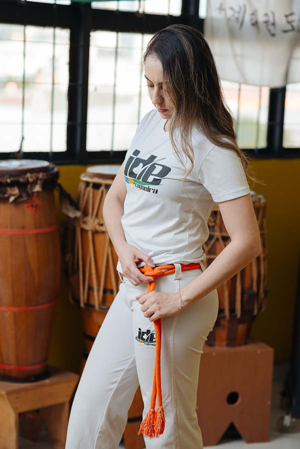Aline ajusta sua corda de capoeira no ensaio pré-casamento com Luidgi. Fotografia lifestyle que une amor e esporte. Registro autêntico e profissional de noivado na academia para inspirar quem busca um ensaio de casamento criativo e temático.