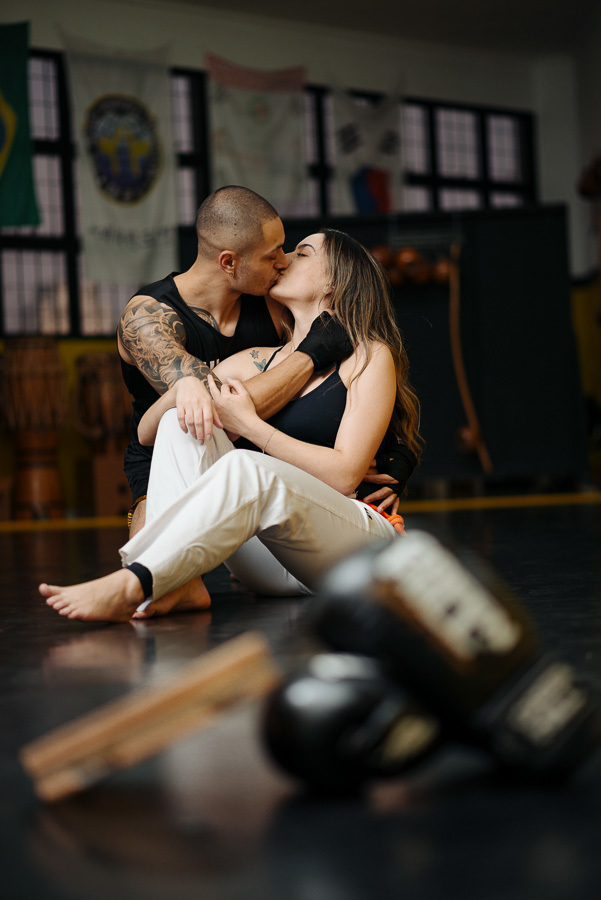 O beijo apaixonado de Luidgi e Aline unindo kickboxing e capoeira. Fotografia de ensaio pré-casamento lifestyle que celebra a história real do casal. Registro profissional e criativo de noivado para inspirar o seu álbum de fotos de casamento.