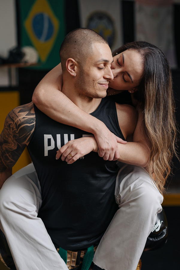 Abraço e sorriso no ensaio pré-casamento de Luidgi e Aline. Fotografia de casal lifestyle que celebra a leveza e a paixão no ambiente de treino. Registro profissional de noivado para casais que buscam autenticidade no álbum de casamento.