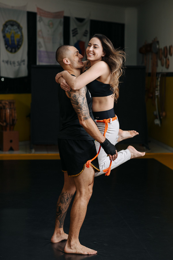 Momento de pura alegria: Luidgi levanta Aline no ensaio pré-casamento lifestyle. Fotografia de noivado autêntica que celebra a conexão e a paixão pelo esporte. Registro profissional e criativo para noivos que buscam um álbum de casamento inesquecível.