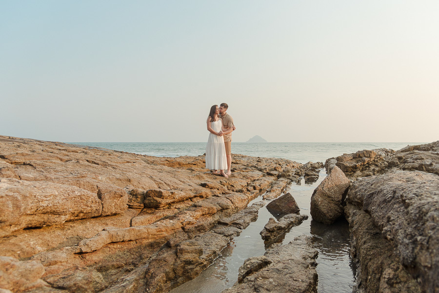 Matthaus e Rebeca em ensaio pré-casamento na Praia de Camburizinho, São Sebastião. Fotografia profissional com o casal posando sobre formações rochosas imponentes à beira-mar, destacando a beleza natural e o horizonte do litoral paulista.