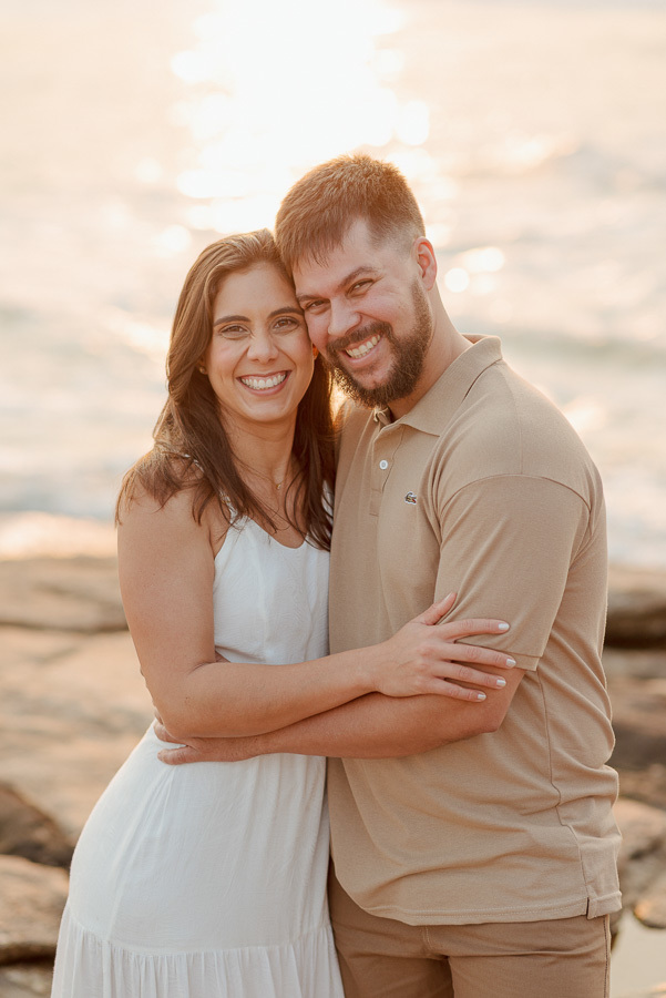 Matthaus e Rebeca caminhando descontraidamente pelas rochas da Praia de Camburizinho. Fotografia de ensaio pré-casamento em São Sebastião, capturando a luz dourada e a paisagem natural do litoral.