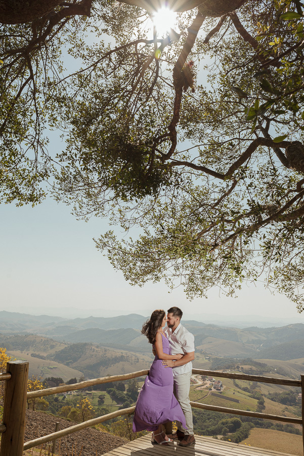O abraço de Matthaus e Rebeca no mirante do Lavandário de Cunha. Ensaio pré-casamento com efeito sun star e vista panorâmica da serra. Fotografia de casal que une a delicadeza do figurino à força da natureza em Cunha, SP. Registro profissional.