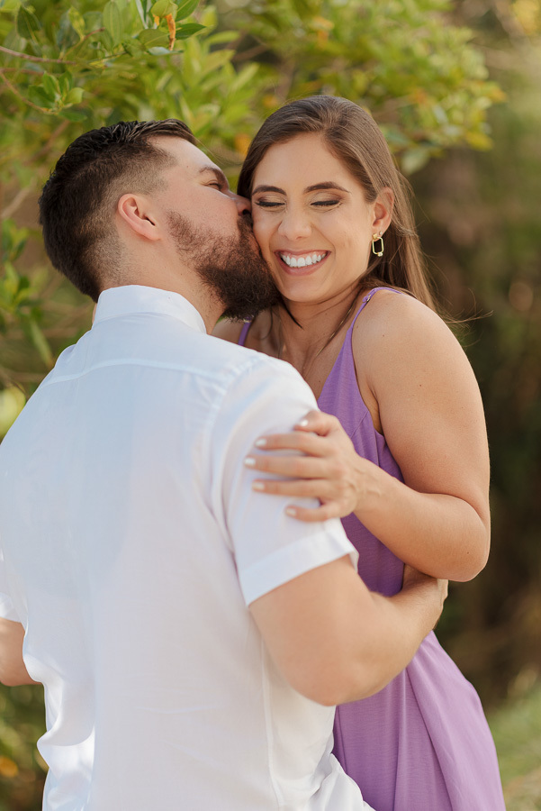 Matthaus beija o rosto de Rebeca em momento de pura felicidade no Lavandário de Cunha. Fotografia de ensaio pré-casamento que celebra a espontaneidade e o amor na serra. Registro profissional, vibrante e cheio de emoção para noivos apaixonados.