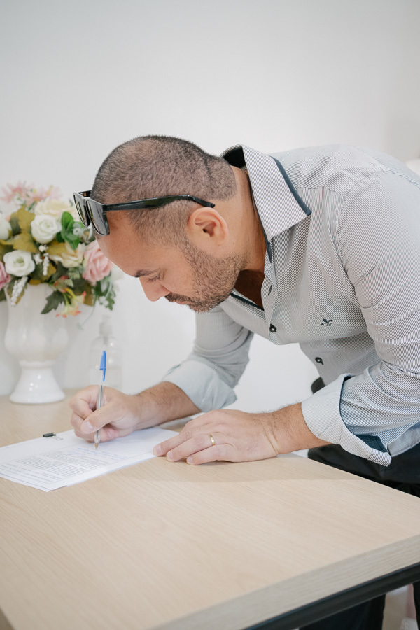 O momento oficial do 'sim': Giovanna e Guilherme assinando o registro de casamento civil no Cartório de Jacareí. Fotografia documental e emocionante.