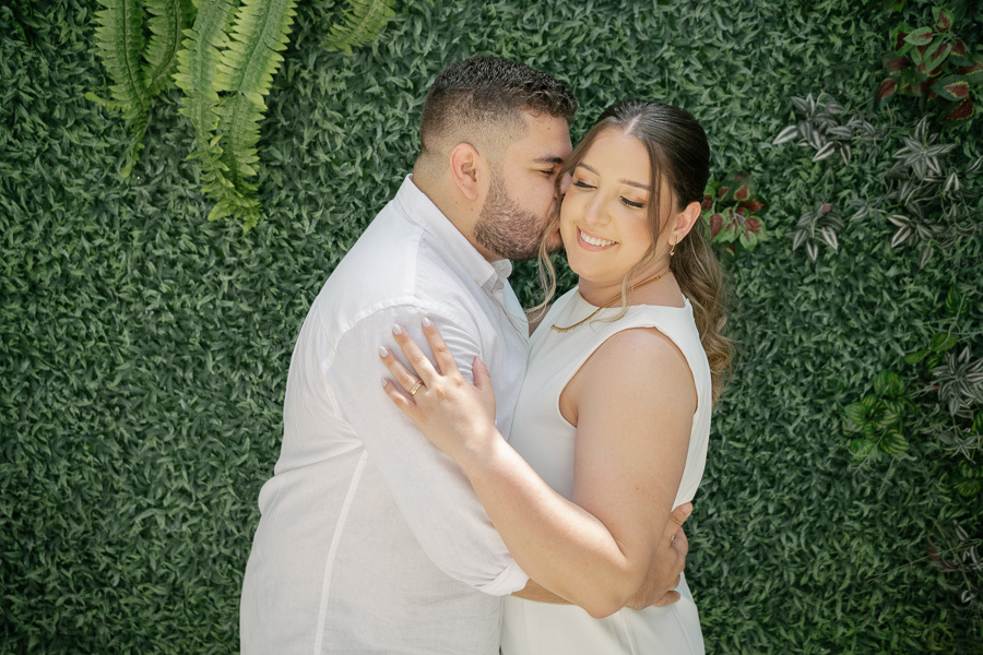 Retrato dos noivos em frente à parede verde. Contraste lindo do branco do vestido com a natureza no registro do casamento civil.