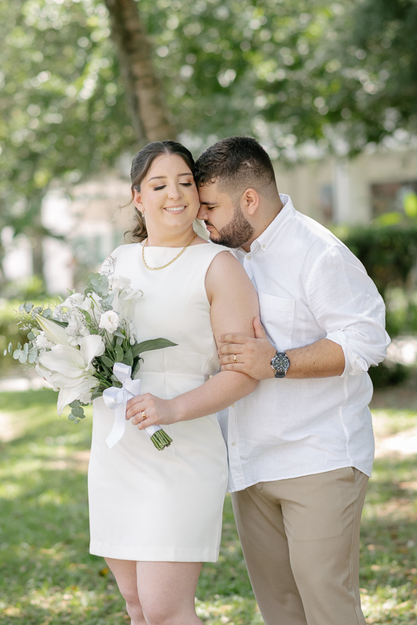 Casal em harmonia: Noivos sorrindo no jardim, com destaque para o buquê de lírios. Fotografia de casamento em São José dos Campos e região.