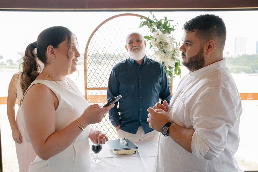 Retrato dos noivos em frente à parede verde. Contraste lindo do branco do vestido com a natureza no registro do casamento civil.