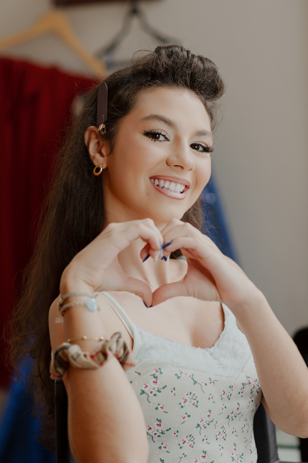 Todo o amor envolvido na celebração. Um close no sorriso radiante da debutante fazendo um coração com as mãos, agradecendo por esse momento especial de 15 anos.